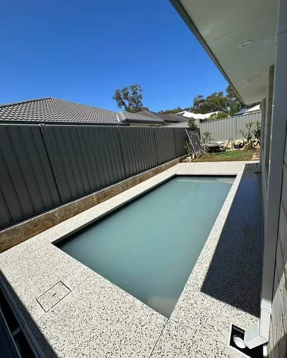 Narrow side yard pool with a white exposed aggregate surround poured right up to the fence line