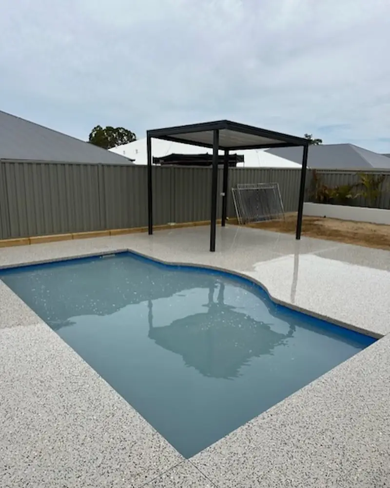 Curved pool with a white exposed aggregate surround and a steel pergola at the far end
