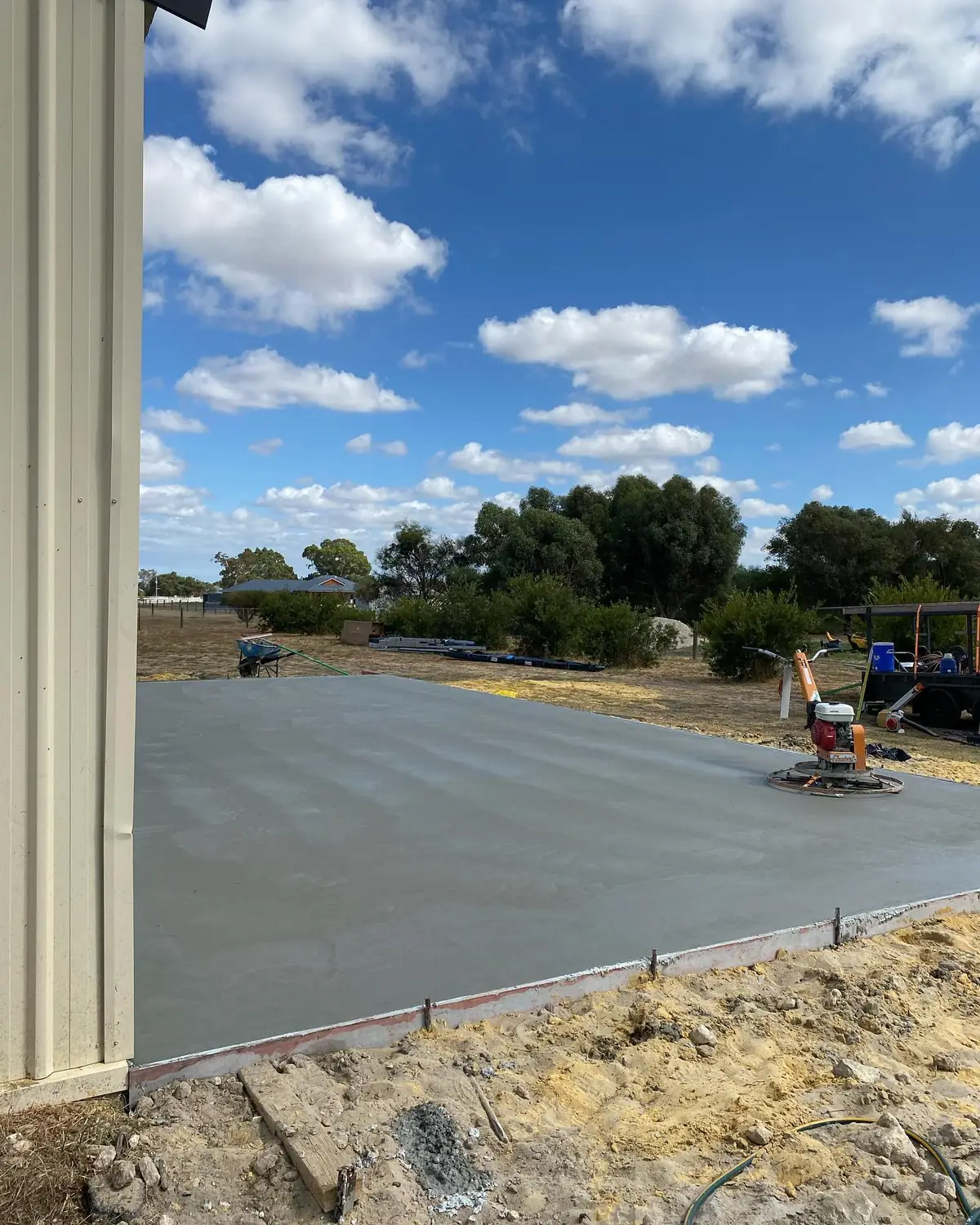 Shed slab just poured, power trowel on the far edge and blue sky over the paddock