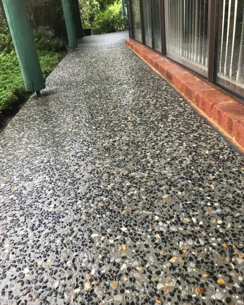 Exposed aggregate path with dark stone through it, running along a brick house with green posts